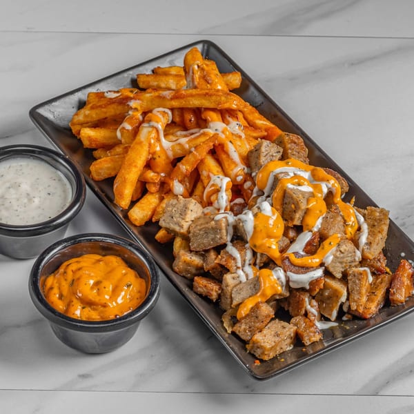 Halal platter with seasoned fries, diced meat, and two sauces on a black tray.