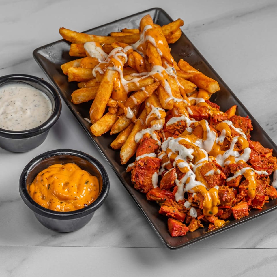 Halal chicken and fries drizzled with white and orange sauces, with two dipping sauces on the side.